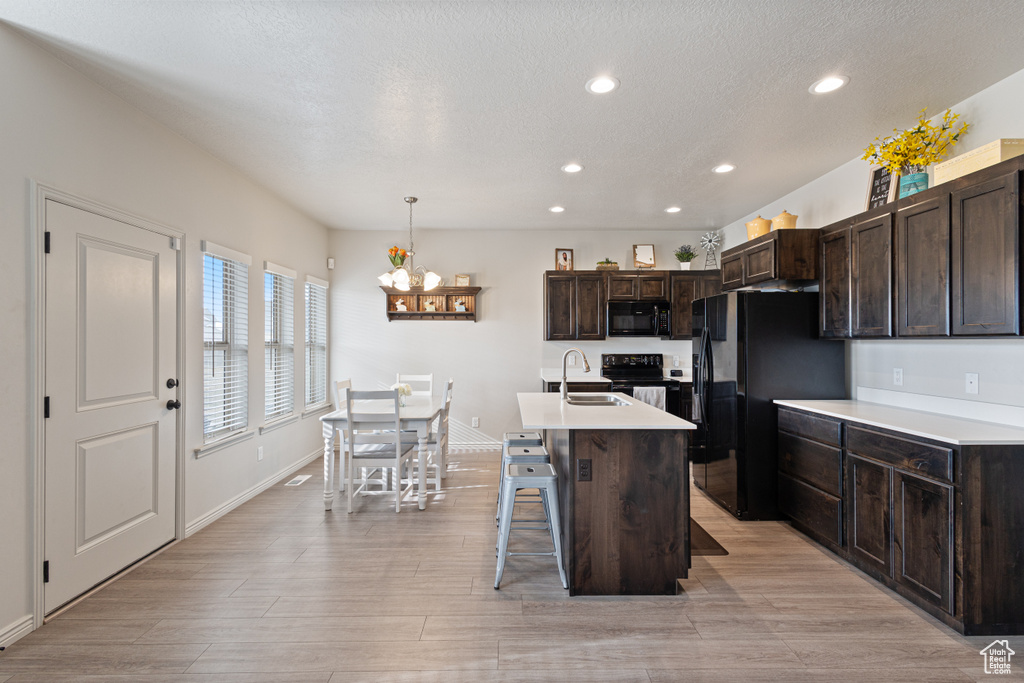 Kitchen with black appliances, an inviting chandelier, a kitchen breakfast bar, decorative light fixtures, and a center island with sink