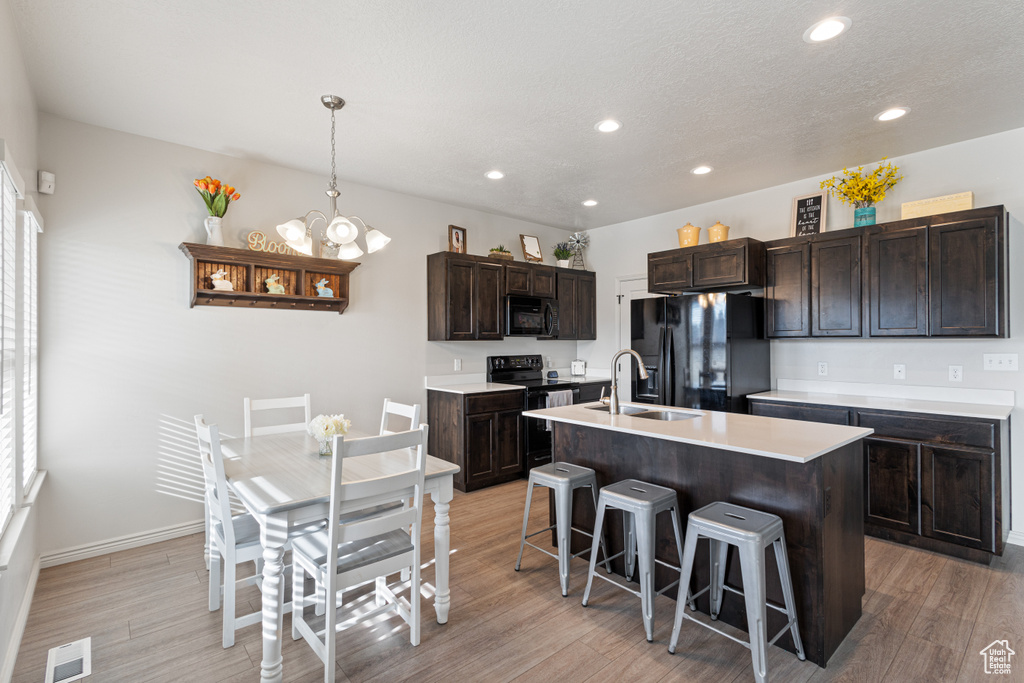Kitchen featuring light hardwood / wood-style floors, a center island with sink, decorative light fixtures, a chandelier, and black appliances