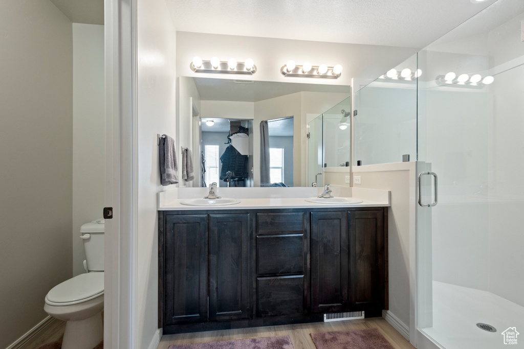 Bathroom with a shower with shower door, hardwood / wood-style floors, dual vanity, and toilet