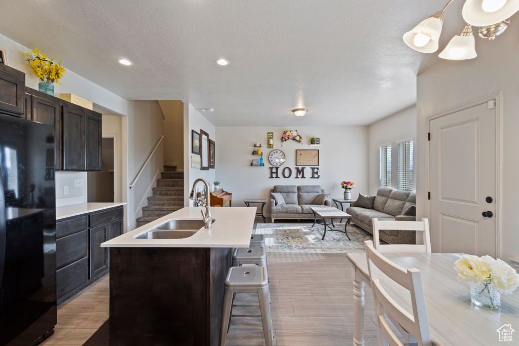 Kitchen featuring light hardwood / wood-style flooring, sink, a breakfast bar area, black refrigerator, and dark brown cabinets