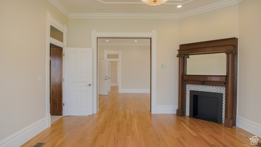 Unfurnished living room featuring a tiled fireplace, ornamental molding, and light hardwood / wood-style floors