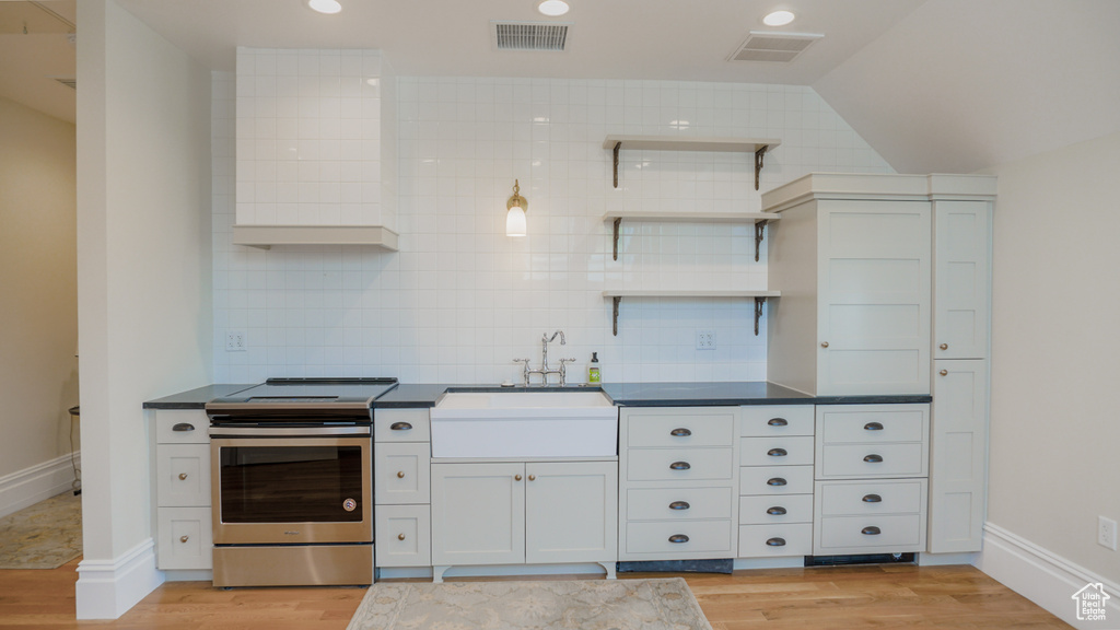 Kitchen with lofted ceiling, stainless steel electric stove, light wood-type flooring, and white cabinets