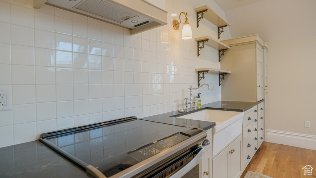 Kitchen with range with electric cooktop, sink, light hardwood / wood-style floors, white cabinetry, and backsplash