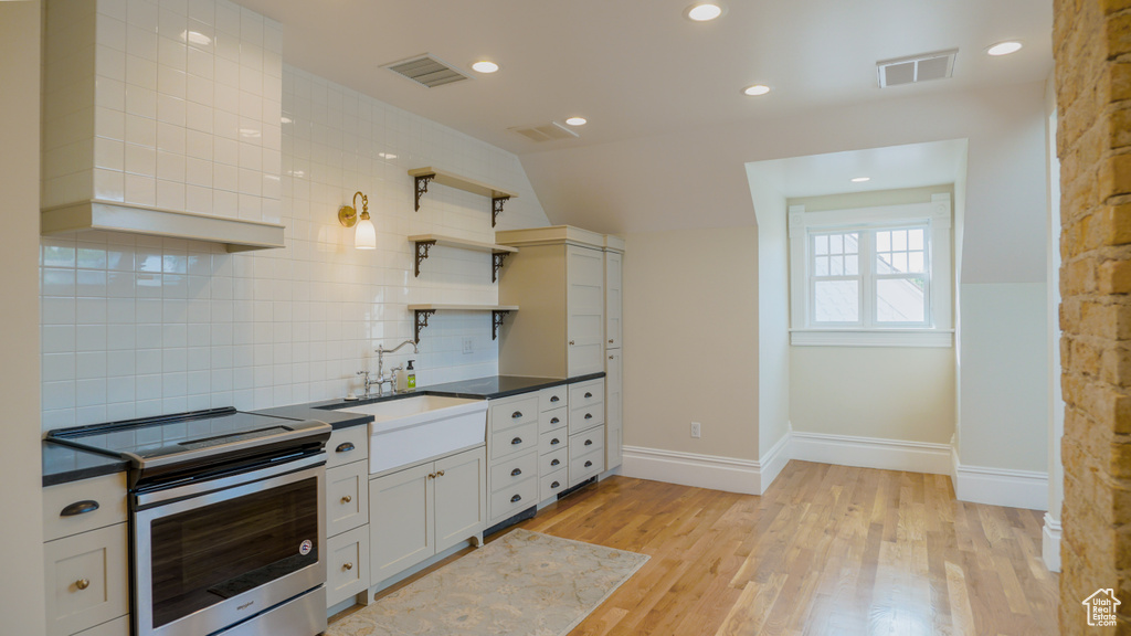 Kitchen with backsplash, electric range, sink, white cabinetry, and light hardwood / wood-style flooring