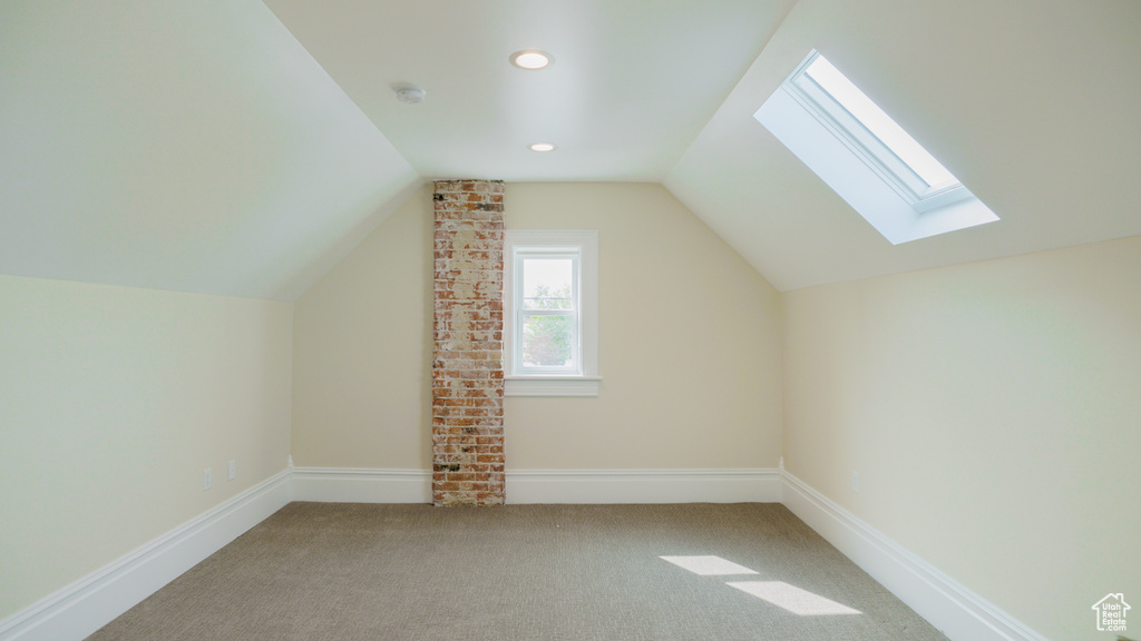 Bonus room with vaulted ceiling with skylight, light colored carpet, and brick wall