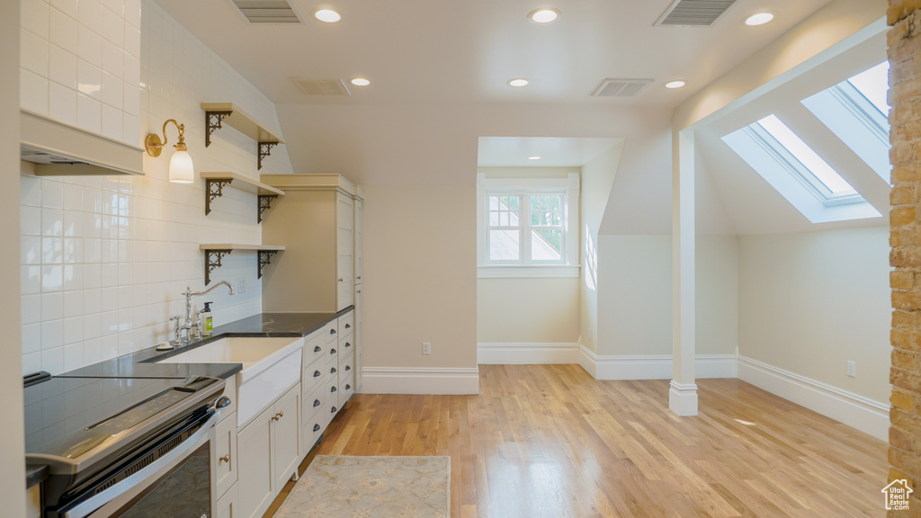 Kitchen featuring white cabinets, lofted ceiling with skylight, light hardwood / wood-style floors, electric range, and backsplash