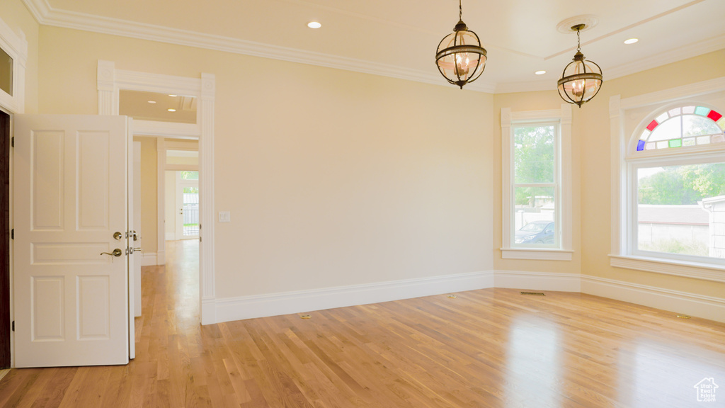 Unfurnished room featuring an inviting chandelier, crown molding, a wealth of natural light, and light hardwood / wood-style floors