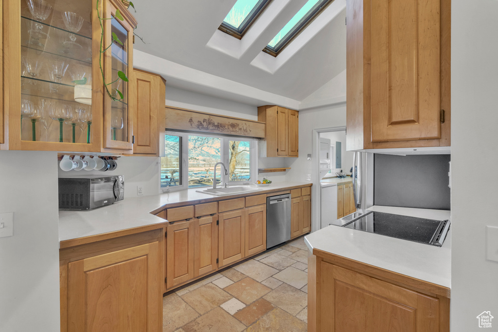 Kitchen with light tile flooring, lofted ceiling with skylight, dishwasher, sink, and light brown cabinetry