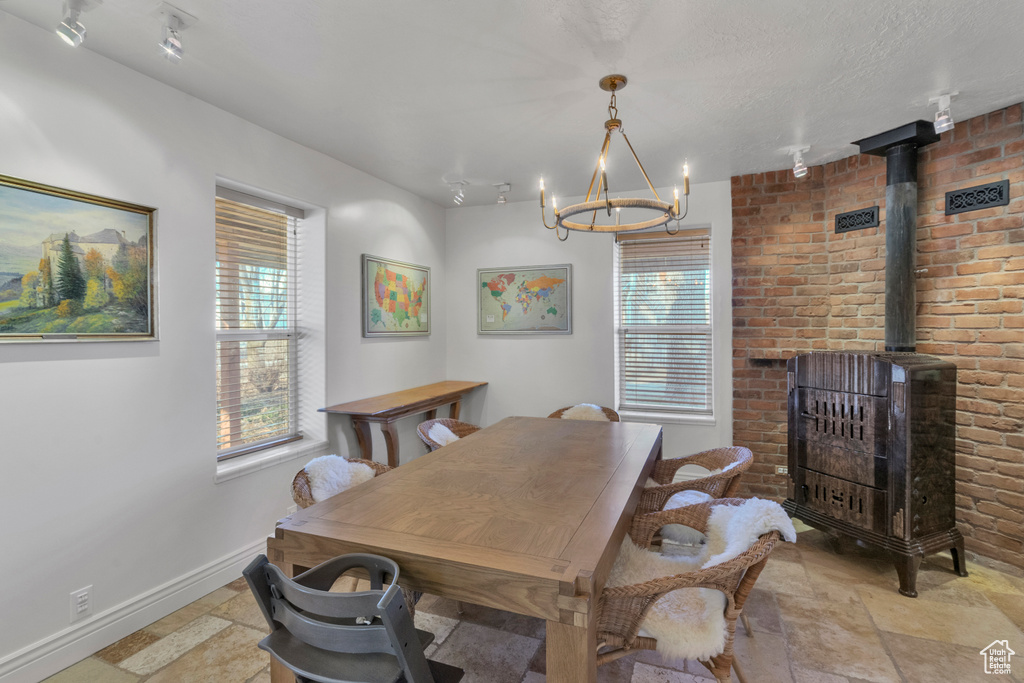 Dining room with a notable chandelier, a wood stove, rail lighting, brick wall, and light tile floors