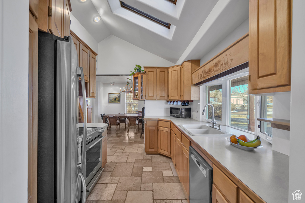Kitchen with appliances with stainless steel finishes, vaulted ceiling with skylight, sink, light tile flooring, and a notable chandelier
