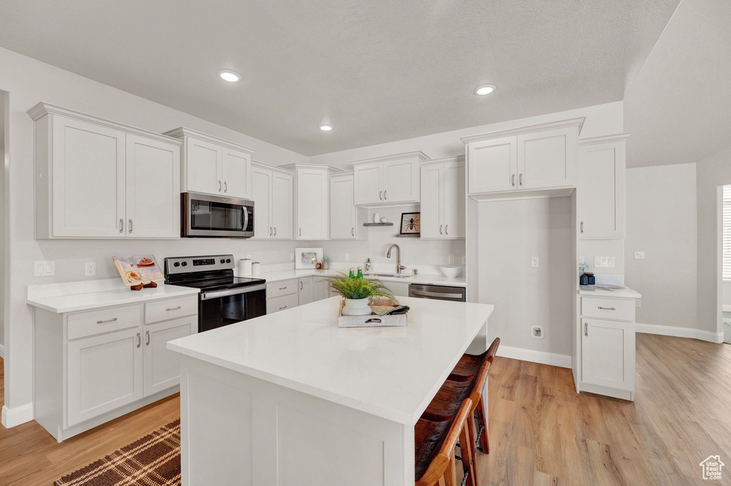 Kitchen with white cabinets, appliances with stainless steel finishes, and light hardwood / wood-style flooring