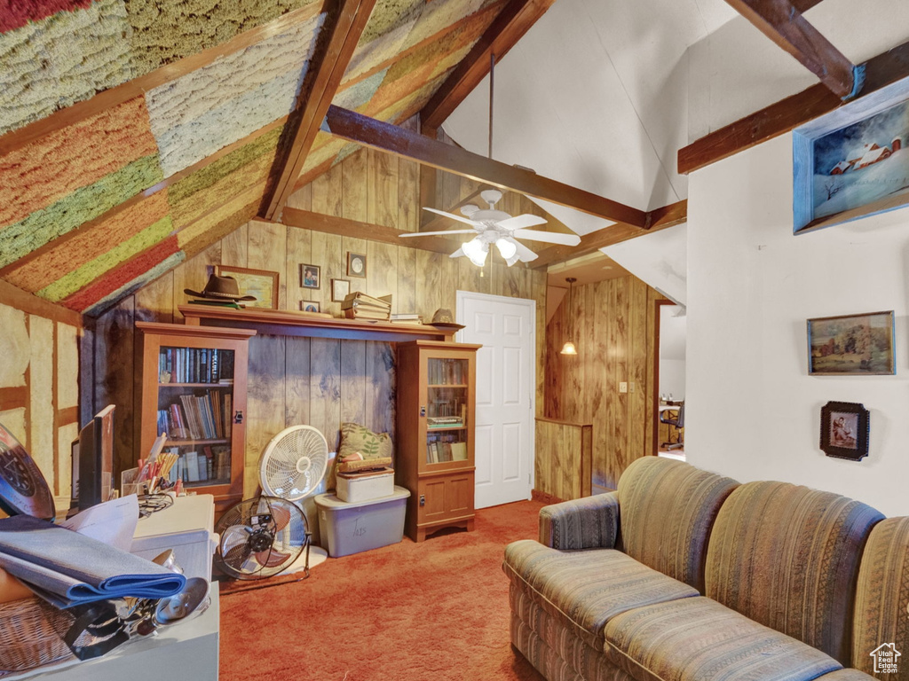 Carpeted living room with ceiling fan, wood walls, and vaulted ceiling with beams