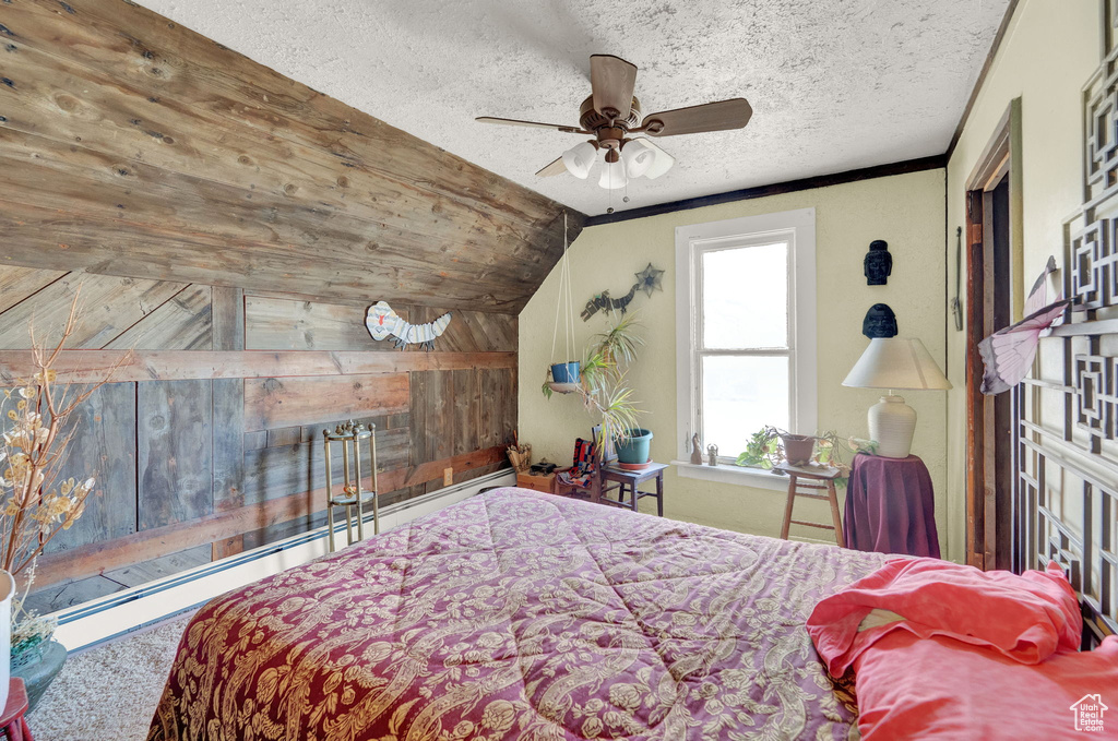 Carpeted bedroom featuring ceiling fan, a baseboard radiator, lofted ceiling, wooden walls, and a textured ceiling