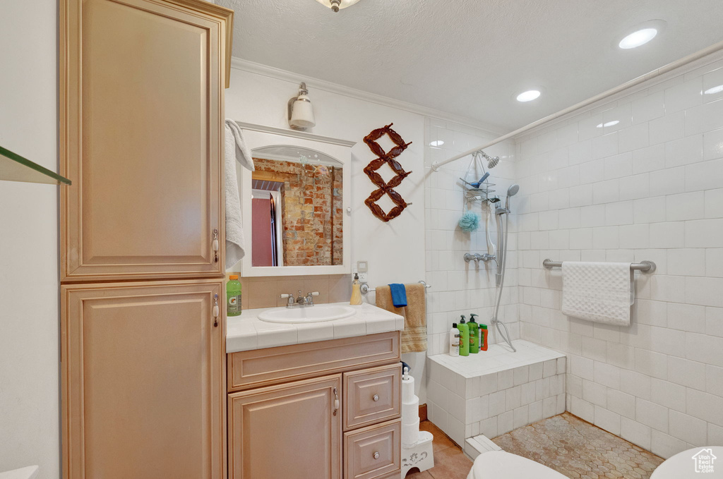 Bathroom with tile walls, tile floors, ornamental molding, large vanity, and a textured ceiling