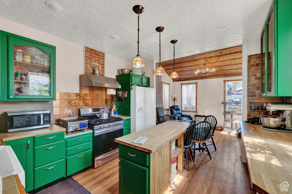 Kitchen with stainless steel appliances, a center island, wall chimney range hood, green cabinetry, and light hardwood / wood-style floors