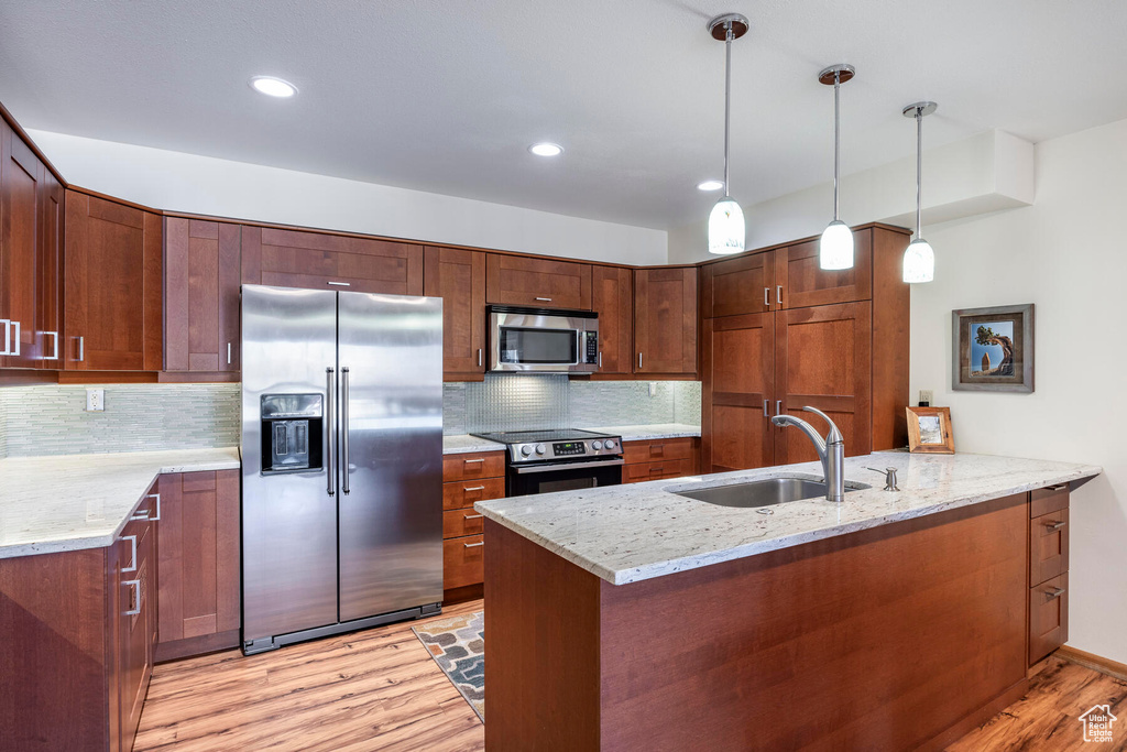 Kitchen featuring pendant lighting, appliances with stainless steel finishes, light stone counters, light hardwood / wood-style flooring, and tasteful backsplash