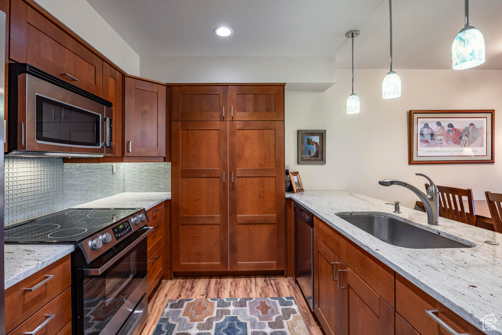 Kitchen with light stone counters, stainless steel appliances, sink, tasteful backsplash, and light hardwood / wood-style floors