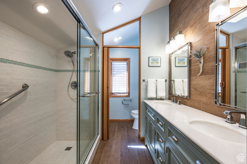 Bathroom featuring hardwood / wood-style floors, tile walls, dual bowl vanity, toilet, and walk in shower