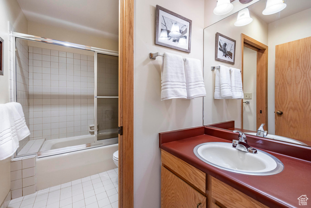 Full bathroom with vanity with extensive cabinet space, shower / bath combination with glass door, toilet, and tile floors