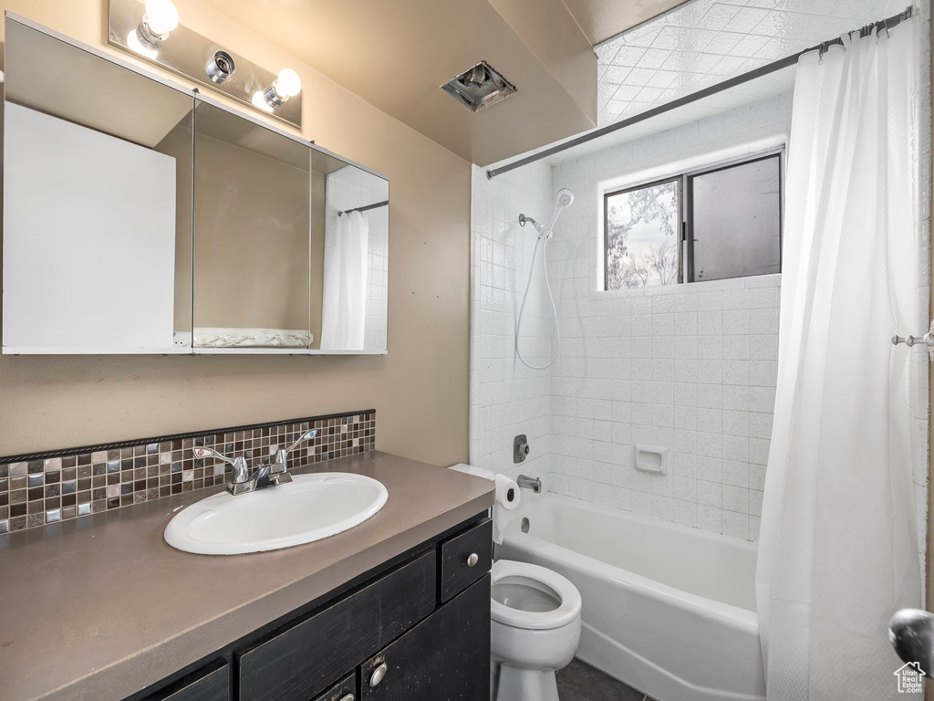 Full bathroom with tasteful backsplash, shower / tub combo with curtain, toilet, and oversized vanity