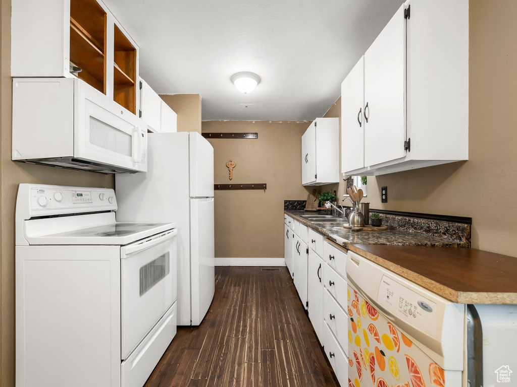 Kitchen featuring white cabinets, sink, white appliances, and dark wood-type flooring