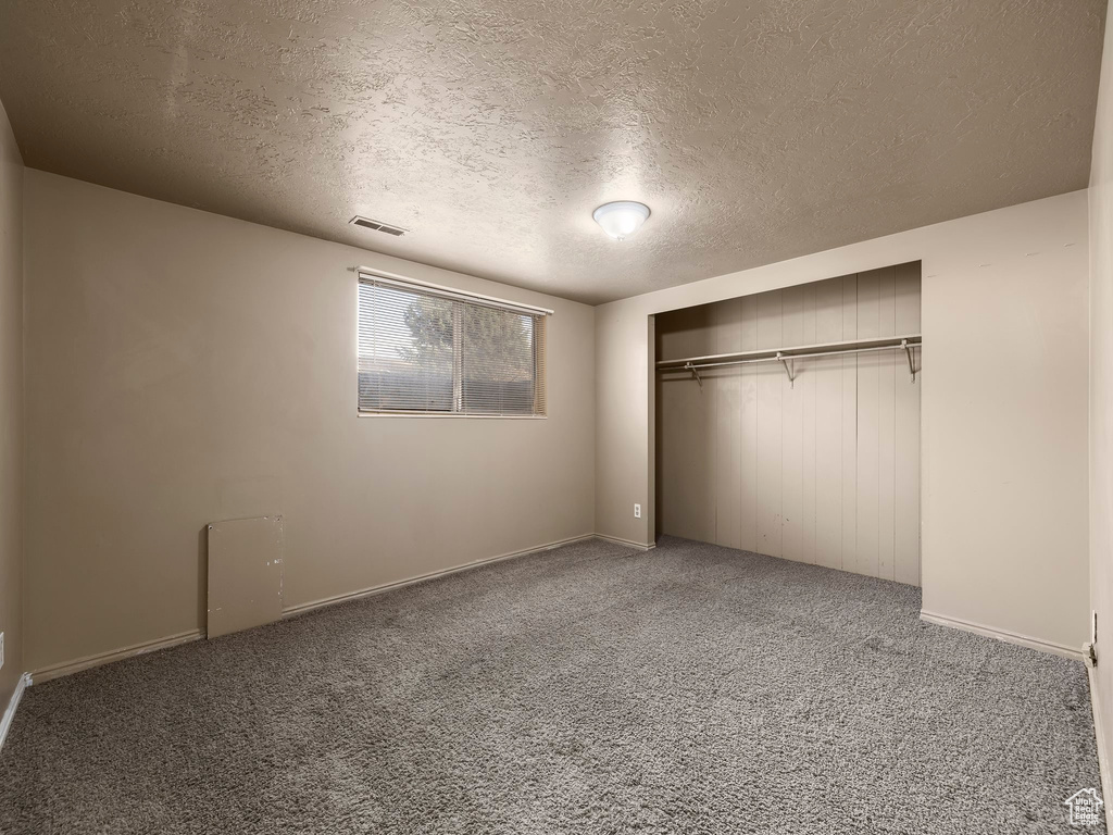 Unfurnished bedroom featuring a closet, a textured ceiling, and carpet