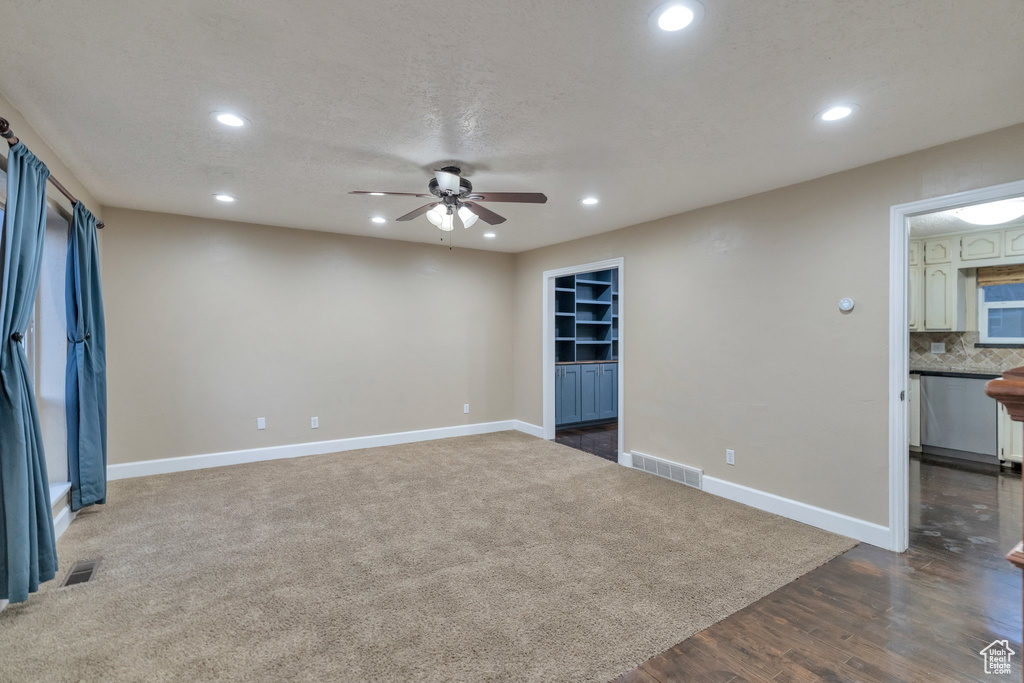 Spare room with a textured ceiling, dark carpet, built in features, and ceiling fan