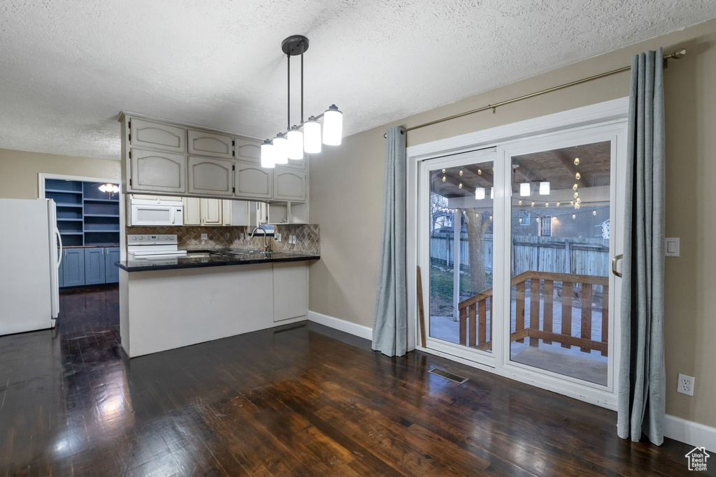 Kitchen featuring hanging light fixtures, white appliances, kitchen peninsula, and dark wood-type flooring