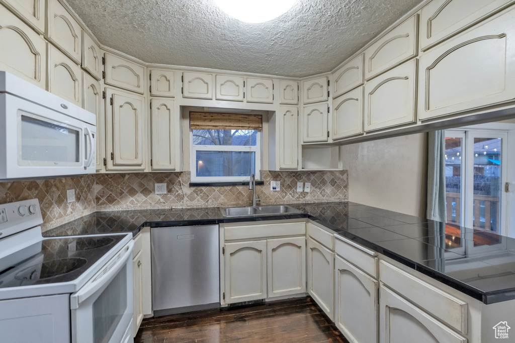 Kitchen featuring a textured ceiling, sink, dark hardwood / wood-style flooring, white appliances, and tasteful backsplash