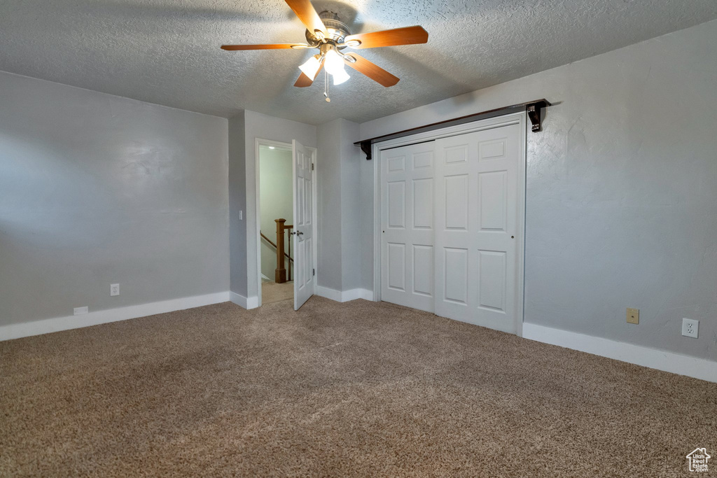 Unfurnished bedroom featuring a textured ceiling, carpet, a closet, and ceiling fan
