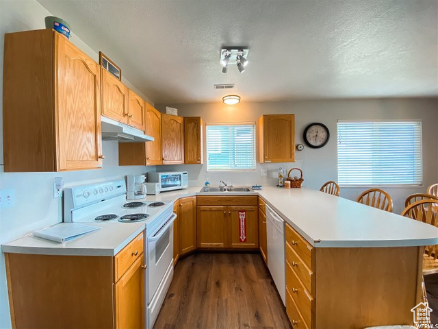 Kitchen featuring kitchen peninsula, dark hardwood / wood-style floors, a breakfast bar, sink, and white appliances