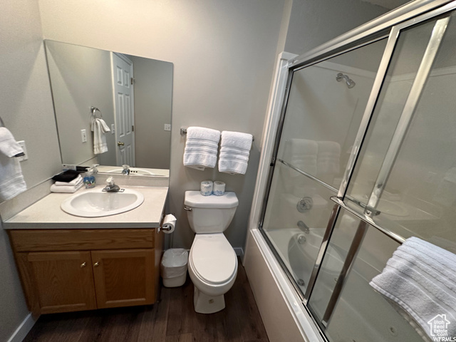 Full bathroom featuring hardwood / wood-style floors, large vanity, toilet, and enclosed tub / shower combo