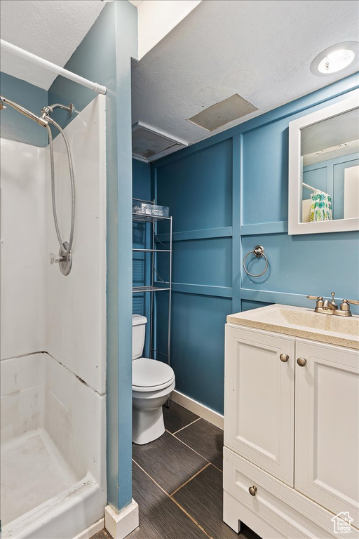 Bathroom with vanity, tile floors, toilet, a shower, and a textured ceiling