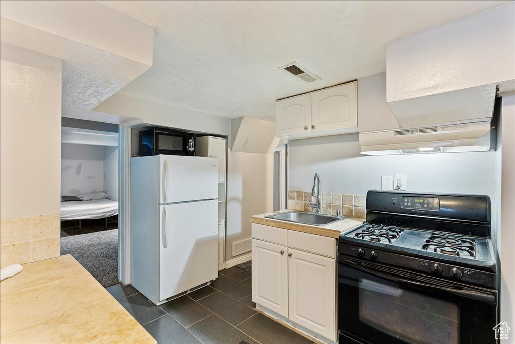 Kitchen with white fridge, black range with gas stovetop, sink, dark tile floors, and premium range hood