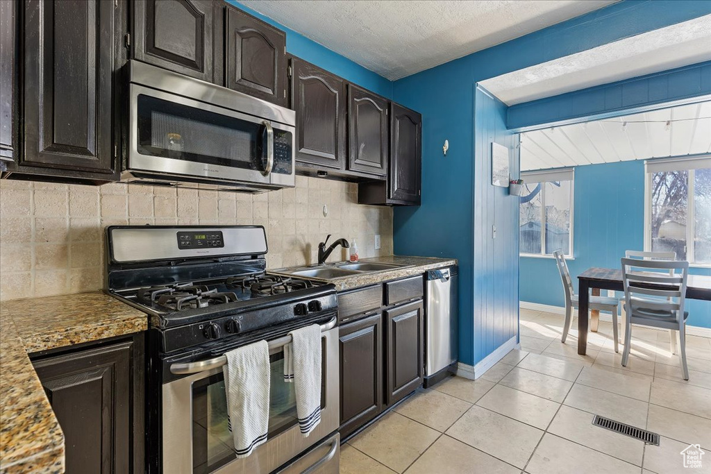 Kitchen featuring appliances with stainless steel finishes, sink, backsplash, and light tile floors