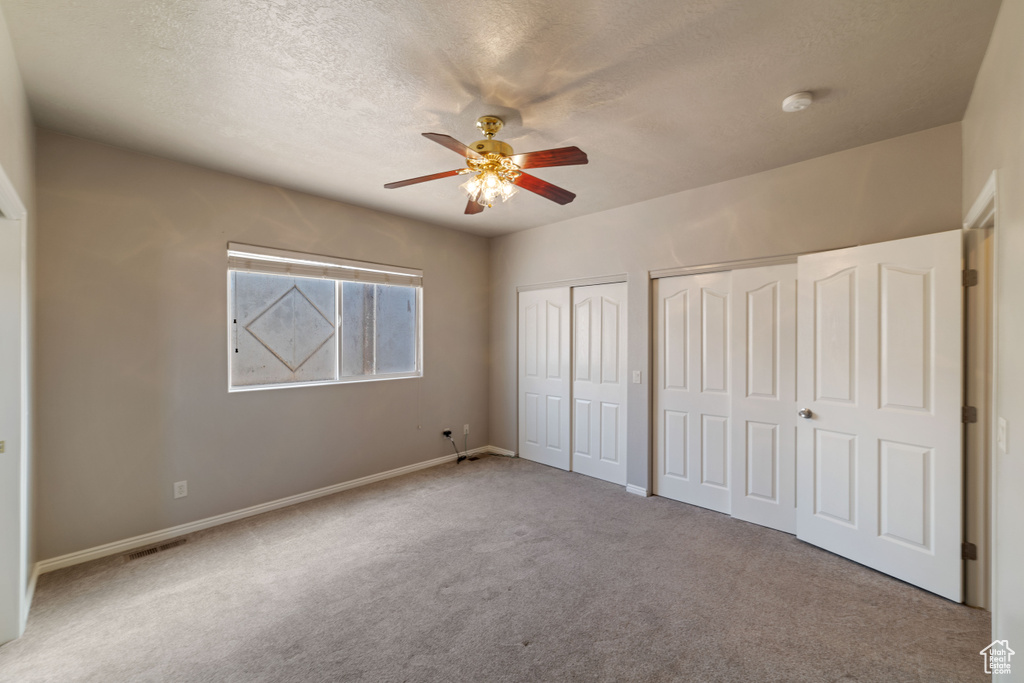 Unfurnished bedroom featuring a textured ceiling, light colored carpet, multiple closets, and ceiling fan