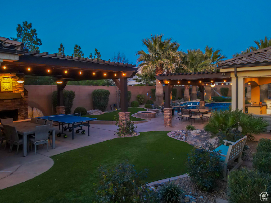 Yard at twilight featuring a patio, an outdoor stone fireplace, and a pergola
