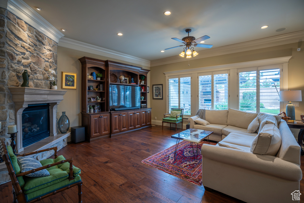 Living room featuring crown molding, dark hardwood / wood-style floors, a stone fireplace, and ceiling fan
