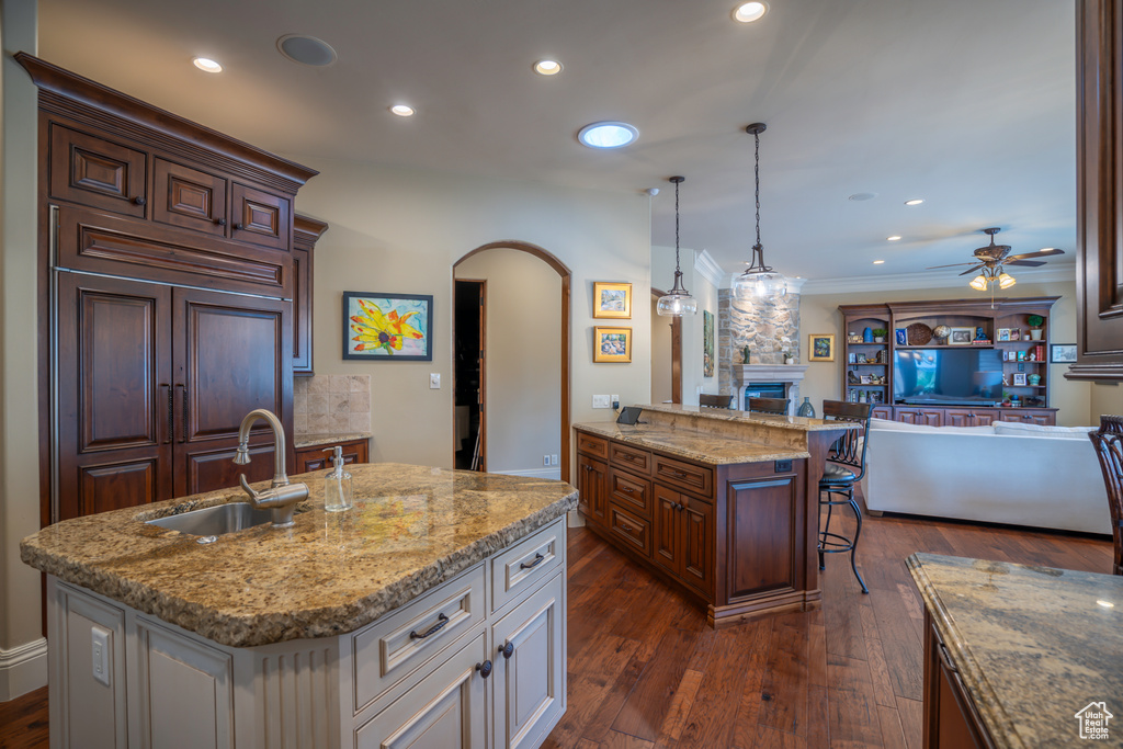 Kitchen featuring a kitchen island with sink, pendant lighting, a kitchen breakfast bar, ceiling fan, and dark hardwood / wood-style flooring