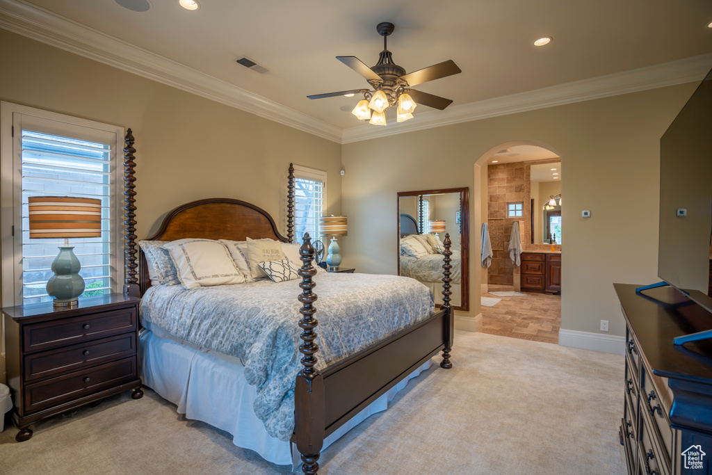 Carpeted bedroom featuring ensuite bath, ceiling fan, crown molding, and multiple windows