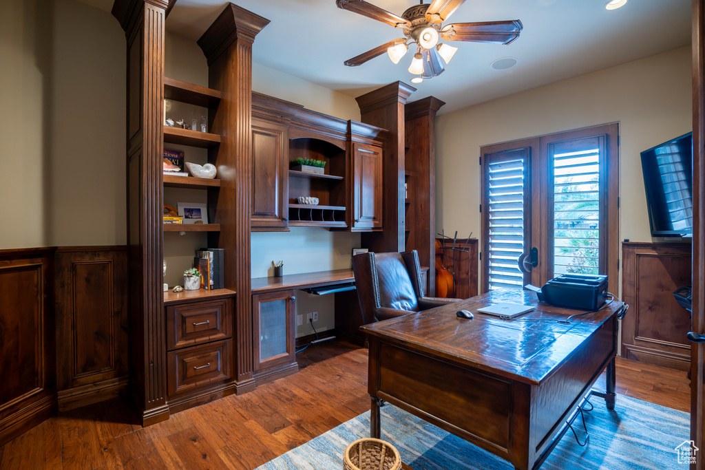 Home office with built in desk, dark wood-type flooring, and ceiling fan