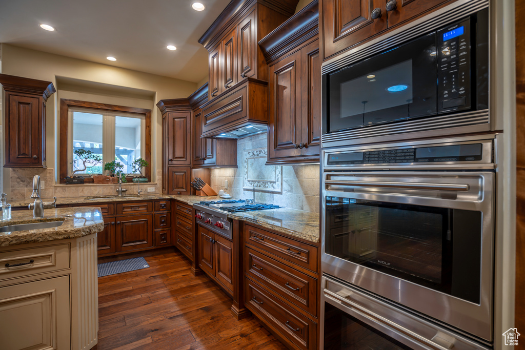 Kitchen with tasteful backsplash, light stone counters, stainless steel appliances, and dark hardwood / wood-style flooring