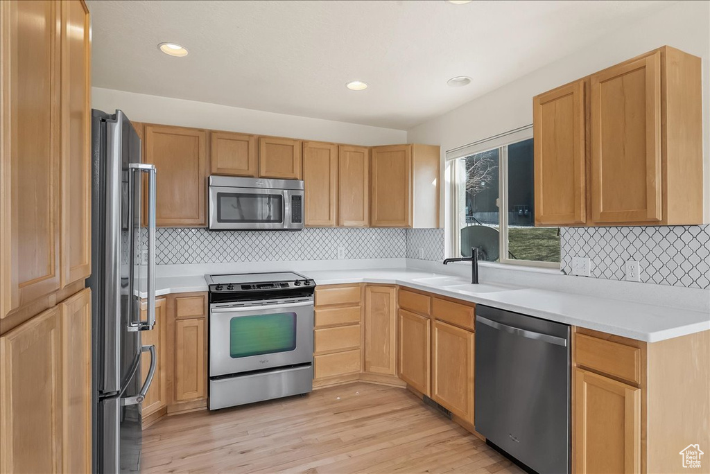 Kitchen with appliances with stainless steel finishes, backsplash, sink, and light hardwood / wood-style floors