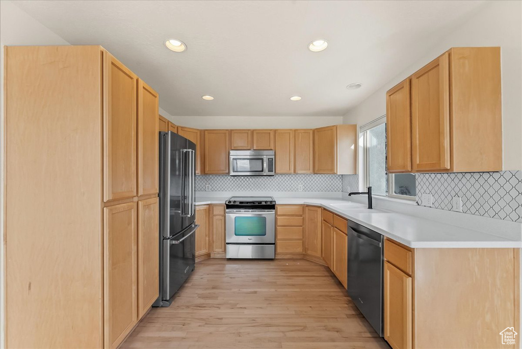 Kitchen with appliances with stainless steel finishes, backsplash, sink, and light hardwood / wood-style floors