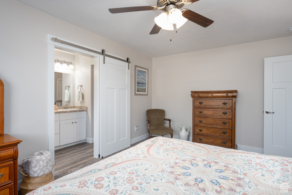 Bedroom with ensuite bathroom, ceiling fan, a barn door, sink, and light hardwood / wood-style floors