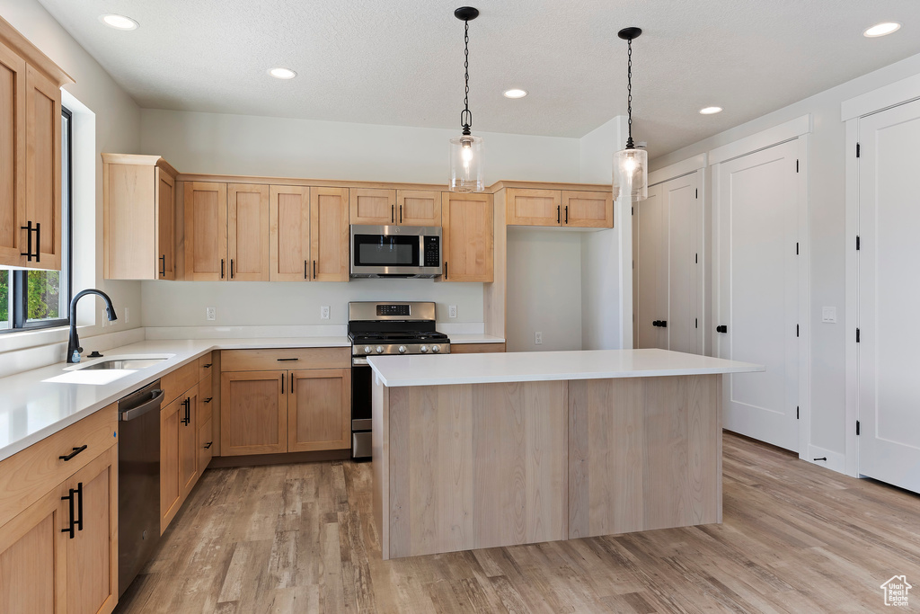 Kitchen featuring light hardwood / wood-style floors, a center island, decorative light fixtures, sink, and appliances with stainless steel finishes
