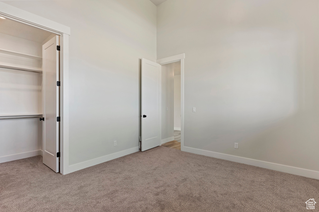 Unfurnished bedroom with a closet, light colored carpet, and a high ceiling