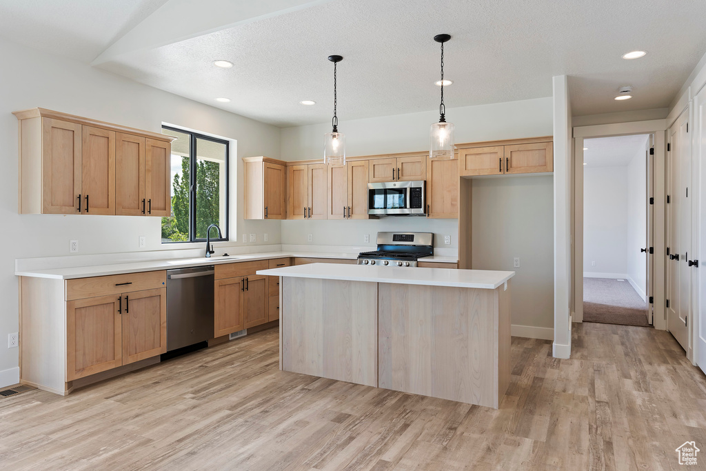 Kitchen featuring light hardwood / wood-style floors, a kitchen island, appliances with stainless steel finishes, and pendant lighting