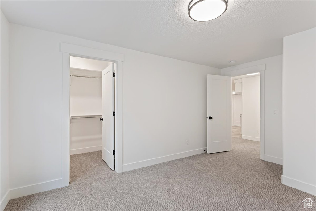 Unfurnished bedroom with a closet, light colored carpet, a textured ceiling, and a walk in closet