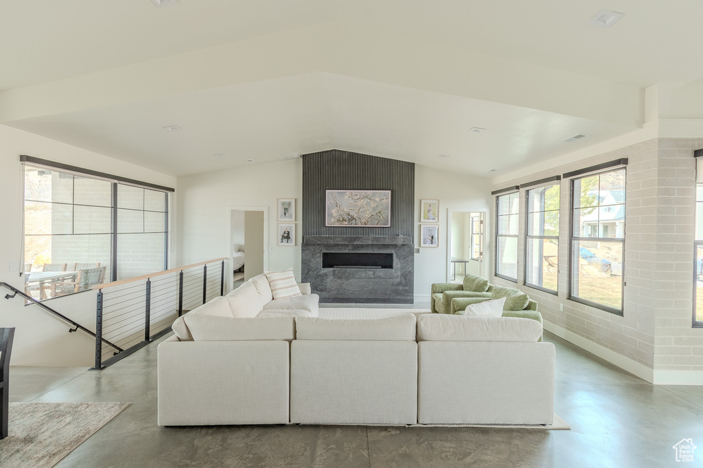 Living room featuring vaulted ceiling, a large fireplace, and concrete floors
